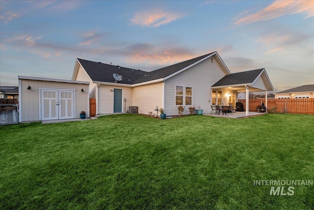 back of house at dusk with fence, a storage shed, a yard, a patio area, and an outbuilding