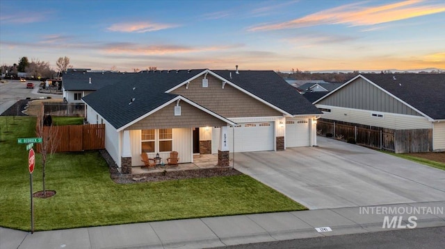 view of front of home with driveway, stone siding, fence, a yard, and an attached garage