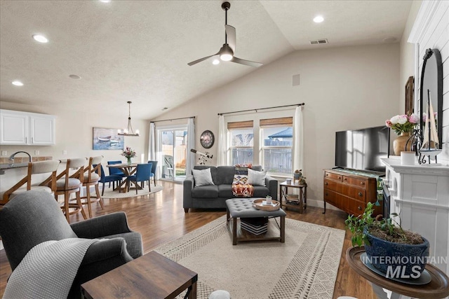 living area with lofted ceiling, a textured ceiling, wood finished floors, and ceiling fan with notable chandelier