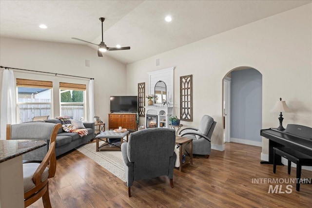 living area featuring baseboards, vaulted ceiling, wood finished floors, arched walkways, and a glass covered fireplace