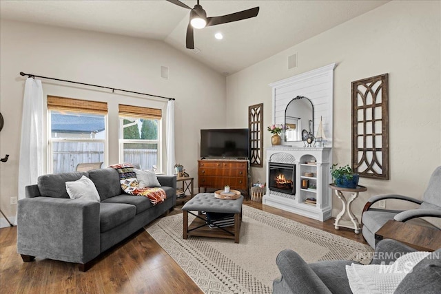 living room featuring visible vents, a ceiling fan, wood finished floors, a glass covered fireplace, and vaulted ceiling