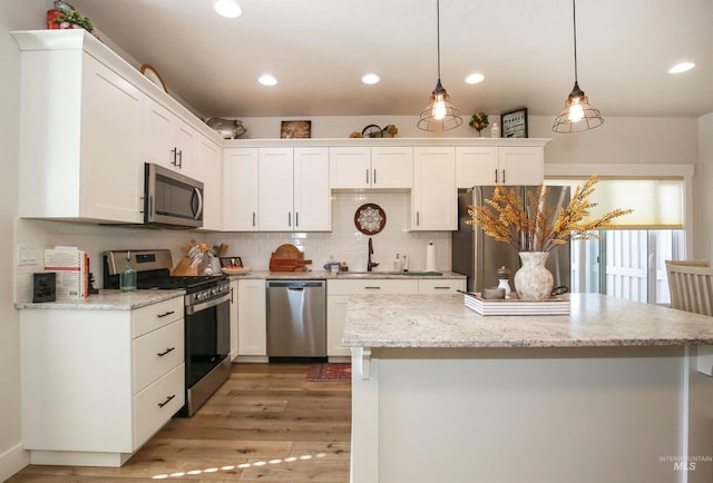 kitchen featuring appliances with stainless steel finishes, light stone countertops, white cabinetry, pendant lighting, and backsplash