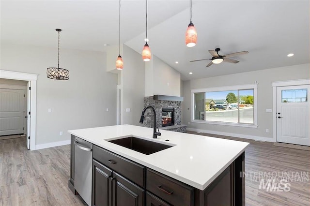 kitchen featuring dishwasher, a sink, open floor plan, a stone fireplace, and vaulted ceiling