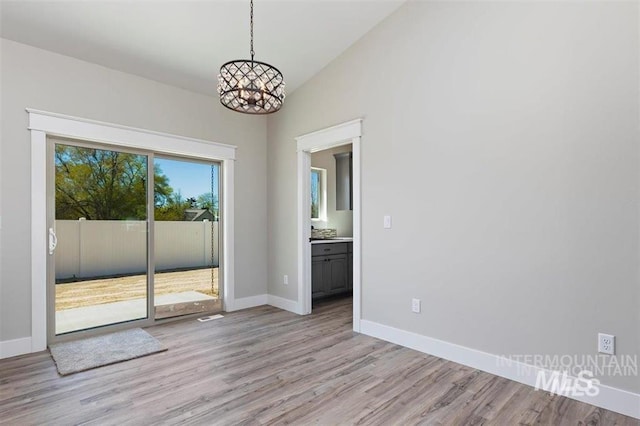 spare room with light wood-style flooring, vaulted ceiling, an inviting chandelier, and baseboards