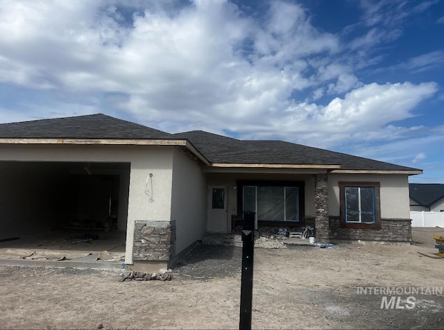 rear view of property with stucco siding, stone siding, and an attached garage