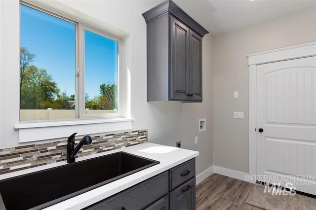 kitchen with light countertops, gray cabinetry, decorative backsplash, a sink, and wood finished floors