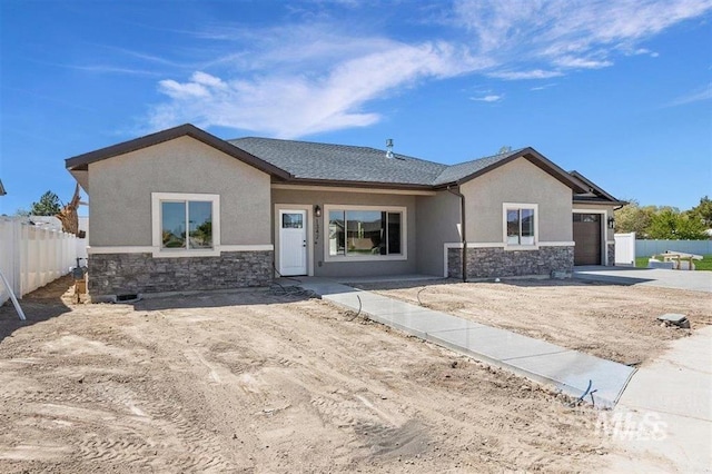 ranch-style house with stucco siding, fence, stone siding, an attached garage, and concrete driveway