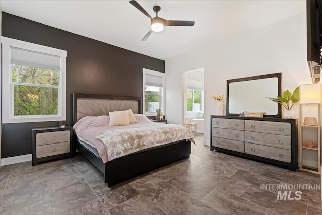 bedroom featuring multiple windows, connected bathroom, a ceiling fan, and baseboards