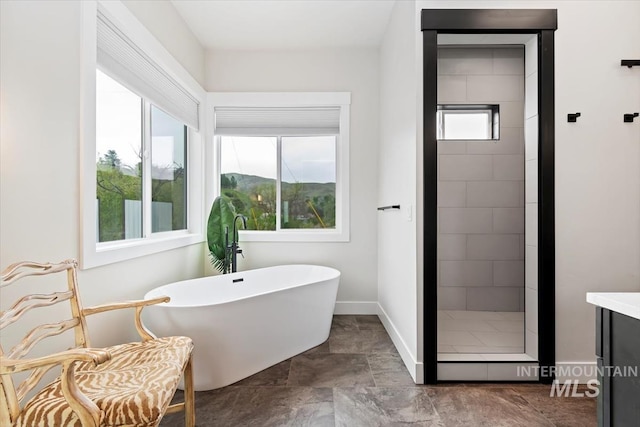 bathroom with a soaking tub, a stall shower, baseboards, and stone finish floors