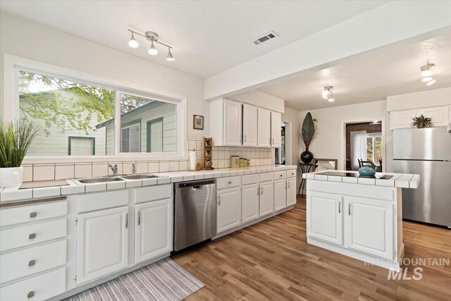 kitchen with appliances with stainless steel finishes, tile countertops, and white cabinets
