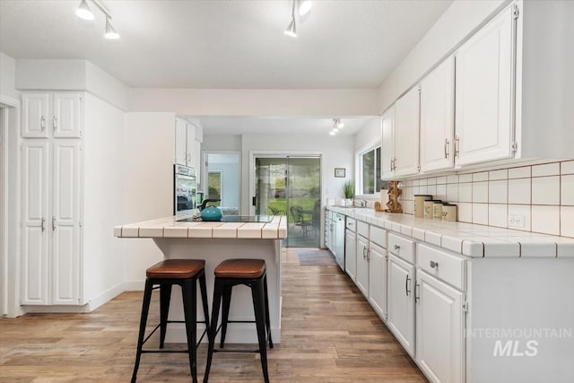 kitchen featuring tile counters, rail lighting, oven, and white cabinetry