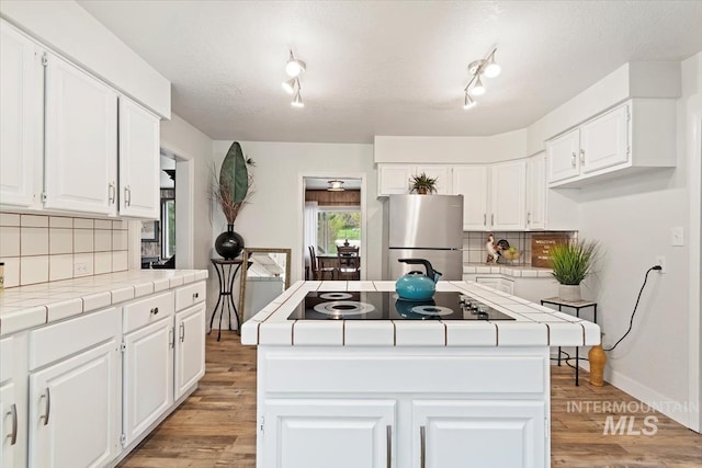 kitchen with freestanding refrigerator, black electric cooktop, tile countertops, and a center island