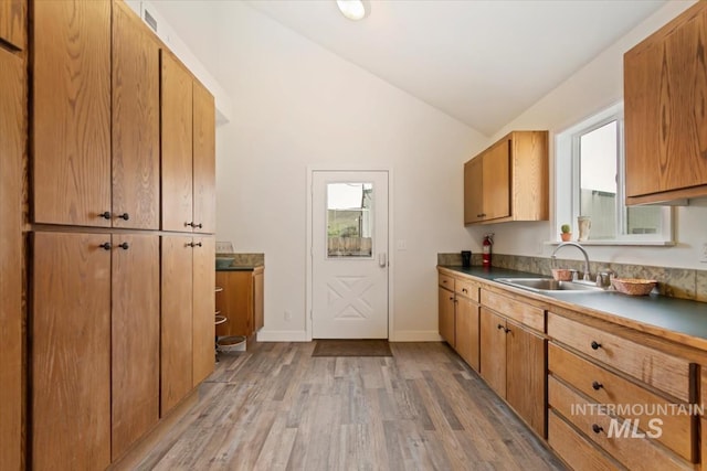 kitchen with lofted ceiling, a sink, light wood-type flooring, brown cabinets, and baseboards