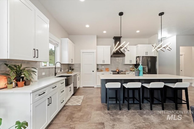 kitchen featuring refrigerator with ice dispenser, wall chimney range hood, a sink, a kitchen island, and a kitchen bar
