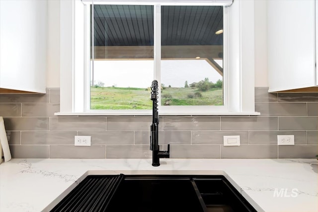 kitchen view of white cabinetry, decorative backsplash, and light stone countertops