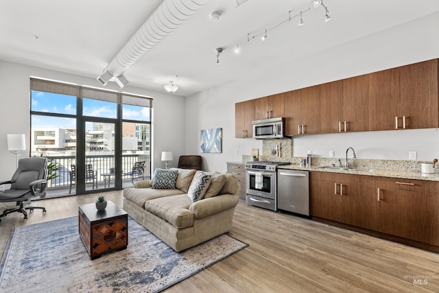 kitchen with light stone counters, appliances with stainless steel finishes, light wood-style floors, open floor plan, and a sink