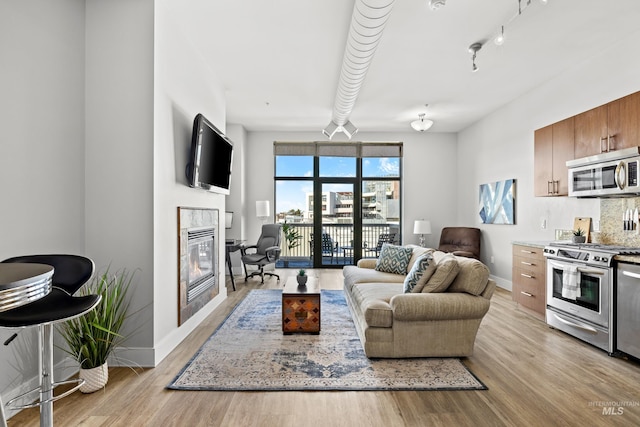 living area featuring a glass covered fireplace, light wood-style flooring, and baseboards