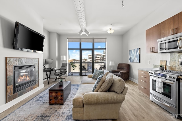 living area with a high end fireplace, light wood-type flooring, and baseboards