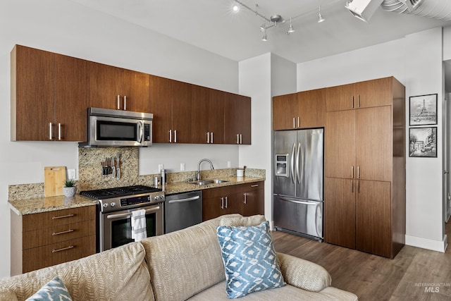 kitchen with dark wood-style flooring, stainless steel appliances, tasteful backsplash, a sink, and light stone countertops