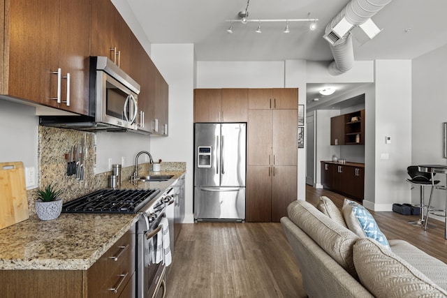 kitchen with appliances with stainless steel finishes, open floor plan, dark wood-type flooring, a sink, and backsplash