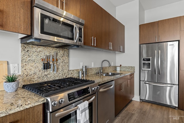 kitchen featuring tasteful backsplash, dark wood finished floors, light stone counters, stainless steel appliances, and a sink