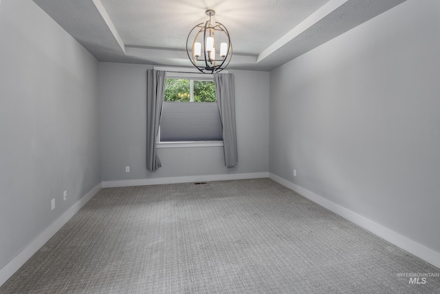 carpeted spare room with a tray ceiling, a chandelier, and baseboards