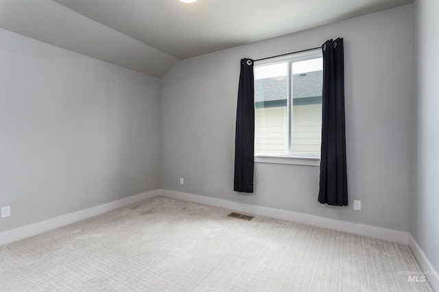 carpeted spare room with vaulted ceiling and baseboards