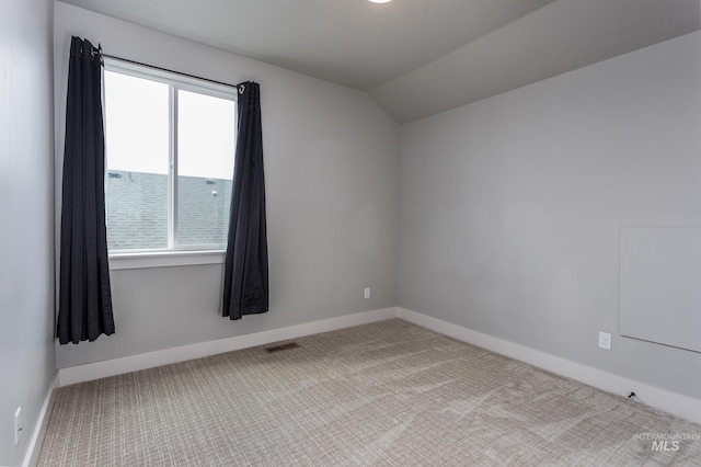 carpeted empty room featuring vaulted ceiling and baseboards