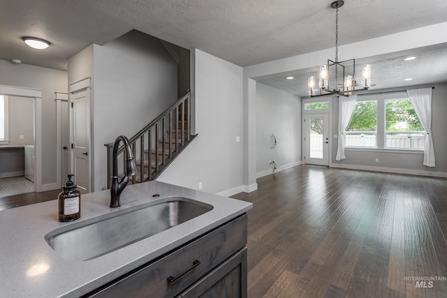 kitchen featuring a sink, a chandelier, a textured ceiling, dark wood-type flooring, and hanging light fixtures