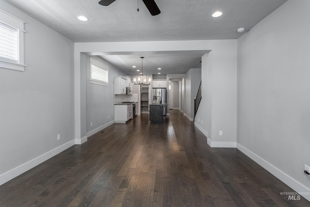unfurnished living room featuring ceiling fan, a chandelier, dark wood-style flooring, baseboards, and recessed lighting