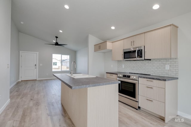 kitchen with a sink, dark countertops, light brown cabinets, light wood-type flooring, and appliances with stainless steel finishes