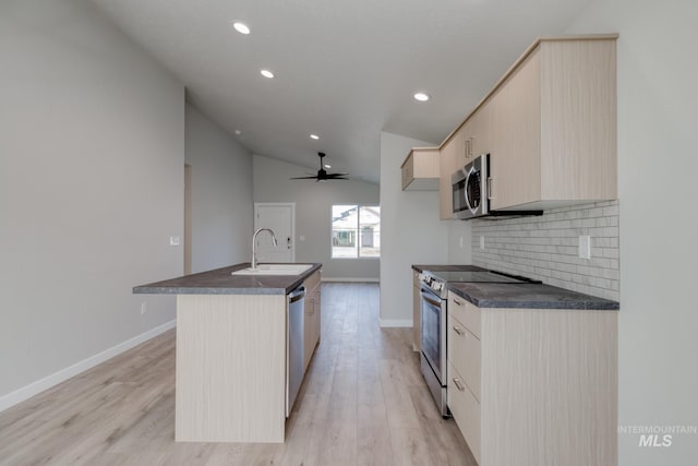 kitchen featuring appliances with stainless steel finishes, light wood-style flooring, a sink, dark countertops, and an island with sink