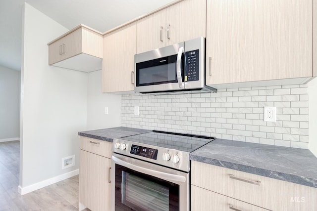 kitchen with appliances with stainless steel finishes, baseboards, light brown cabinets, and backsplash