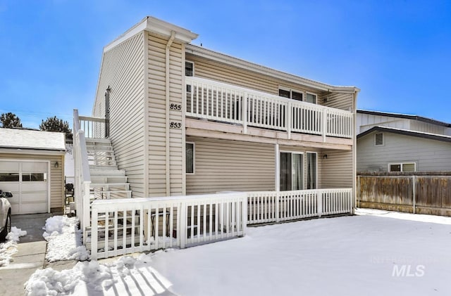 snow covered rear of property with a garage and a balcony