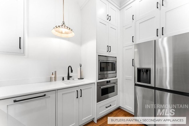 kitchen with stainless steel appliances, wood finished floors, a sink, white cabinetry, and light countertops