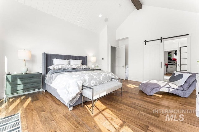 bedroom featuring a barn door, wood finished floors, beamed ceiling, a walk in closet, and high vaulted ceiling