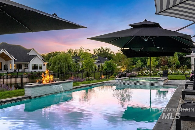 pool at dusk featuring a pool with connected hot tub and fence