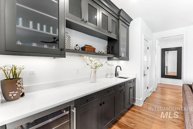 bar with indoor wet bar, a sink, light wood-type flooring, beverage cooler, and baseboards