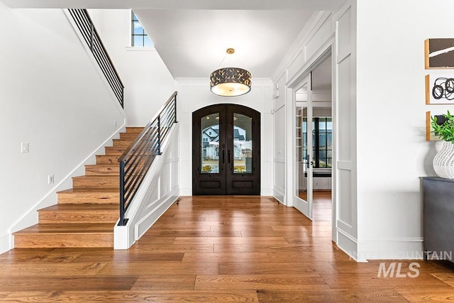 foyer with stairs, arched walkways, french doors, and wood finished floors