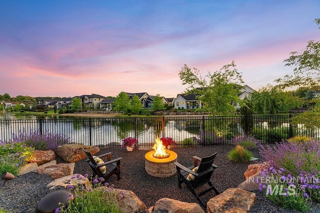 patio terrace at dusk with a residential view, a fenced backyard, a water view, and a fire pit