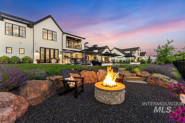 back of house at dusk with a patio area, a fire pit, a balcony, and stucco siding