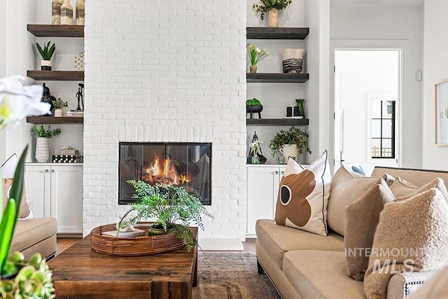 living room featuring a brick fireplace, visible vents, built in features, and wood finished floors