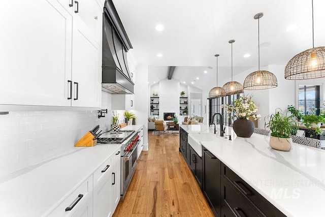 kitchen featuring range with two ovens, white cabinets, a sink, light wood-type flooring, and premium range hood