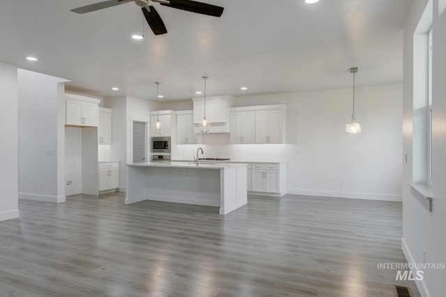 kitchen with appliances with stainless steel finishes, a center island with sink, white cabinetry, and light hardwood / wood-style flooring