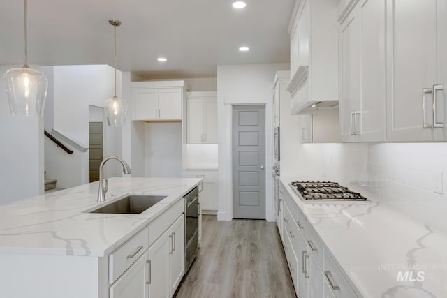 kitchen with white cabinets, decorative light fixtures, a kitchen island with sink, and sink