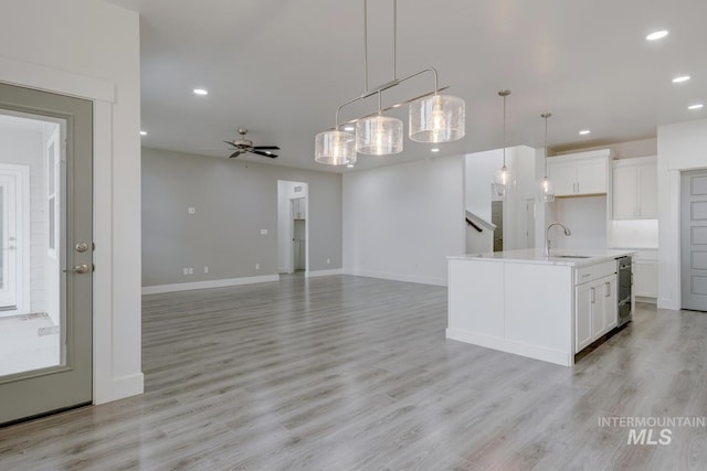 kitchen with light wood-type flooring, decorative light fixtures, a kitchen island with sink, and sink