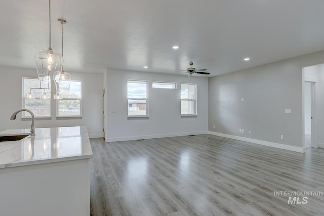 unfurnished living room with ceiling fan, sink, a wealth of natural light, and light hardwood / wood-style flooring