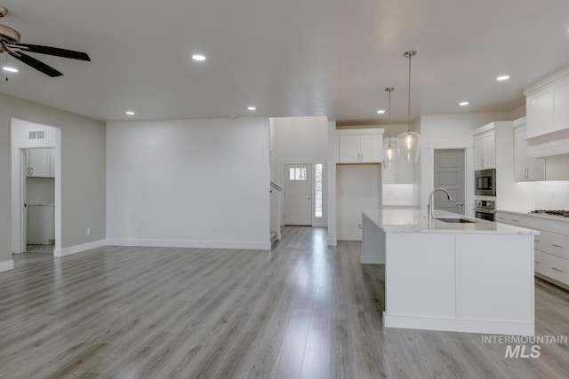 kitchen featuring a kitchen island with sink, white cabinets, hanging light fixtures, light hardwood / wood-style flooring, and stainless steel appliances