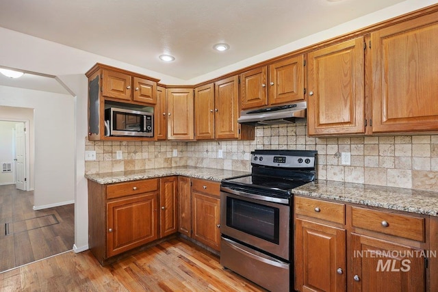 646 W Falls Ave, Twin Falls, ID 83301 - kitchen with stainless steel appliances, under cabinet range hood, brown cabinets, light stone countertops, and light wood finished floors