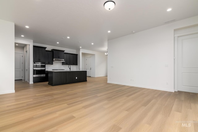 2386 N Leatherwood Ave, Star, ID 83669 - kitchen with under cabinet range hood, open floor plan, a kitchen island with sink, light wood finished floors, and recessed lighting